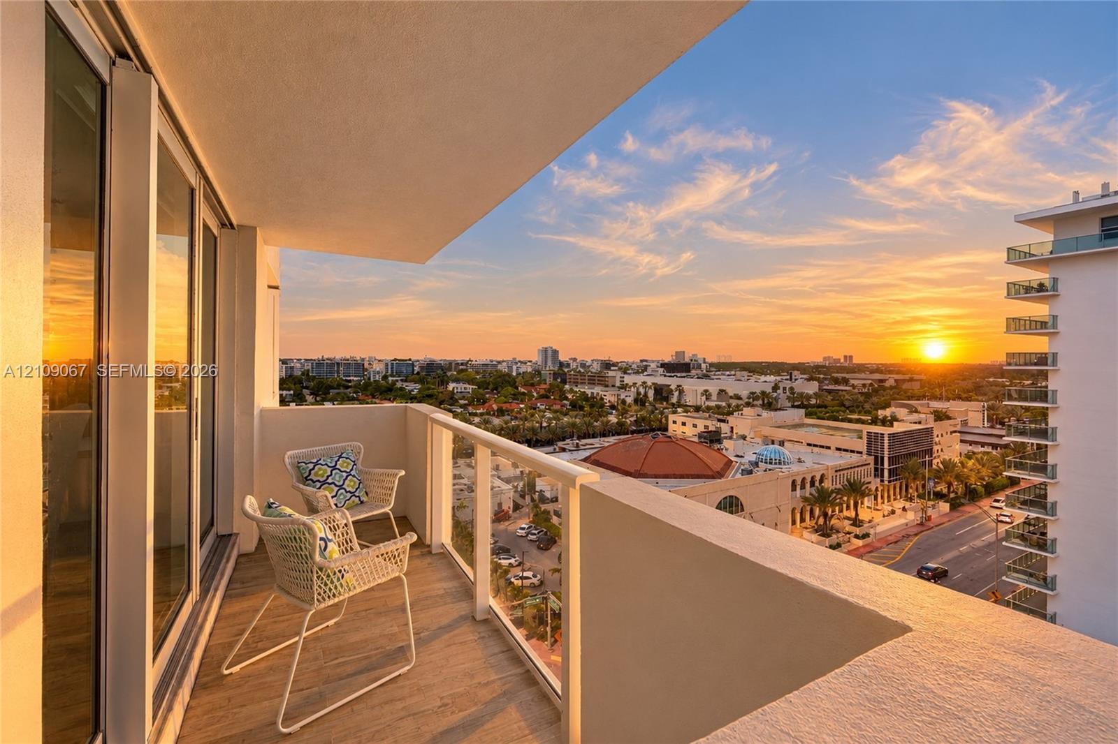 Covered balcony featuring wood-finish flooring and glass panel railing, complemented by expansive urban scenery and horizon sunset