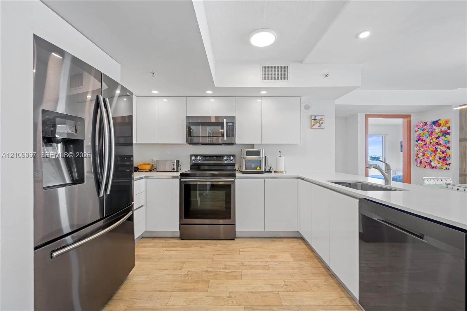 Kitchen featuring white flat-panel cabinetry, quartz countertops, stainless steel appliances, and wood-finish flooring Kitchen featuring white flat-panel cabinetry, quartz countertops, stainless steel appliances, and wood-finish flooring