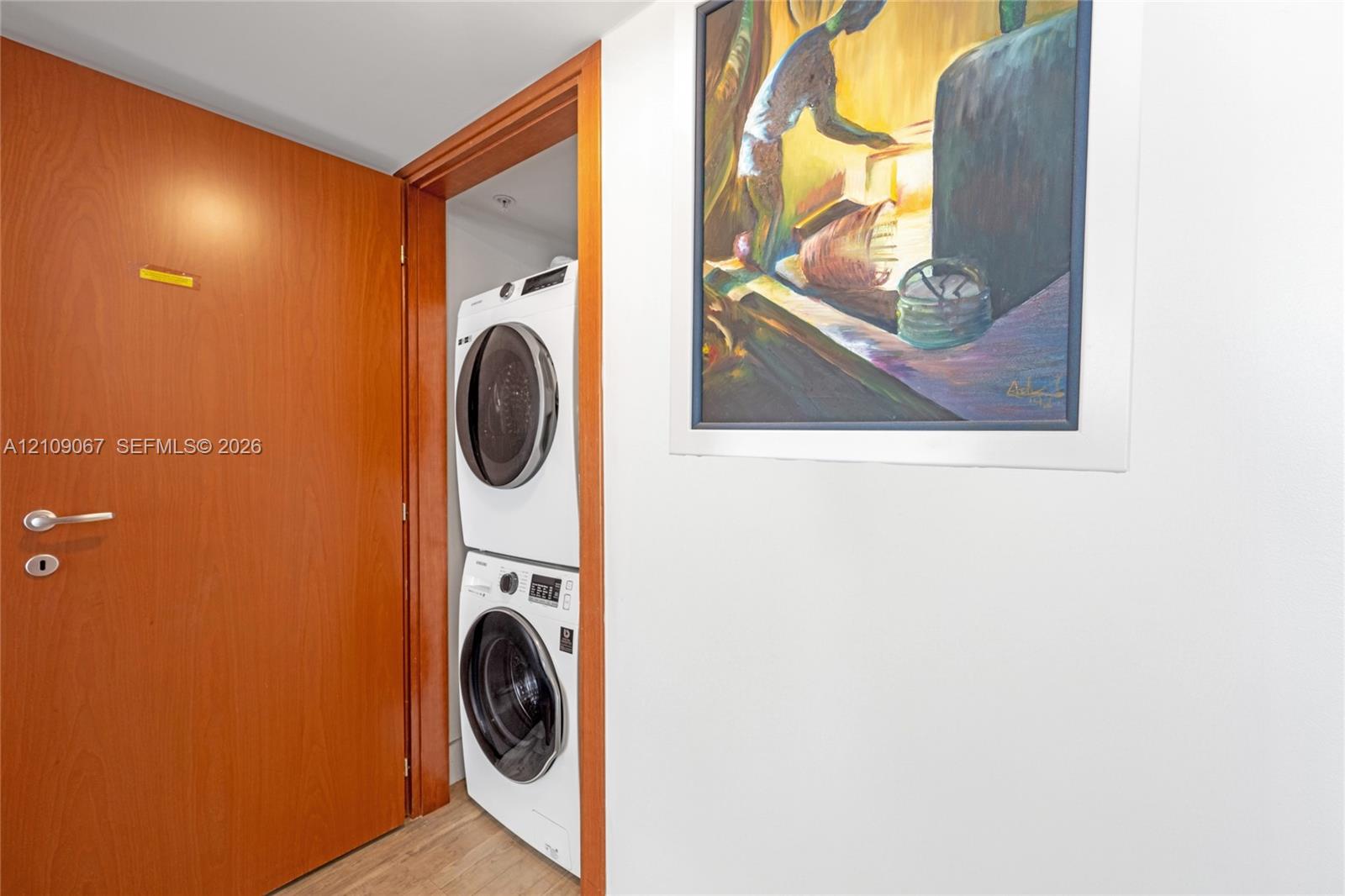 Laundry alcove featuring a stacked white washer and dryer unit, wood-finish interior door, and door frame with natural wood trim