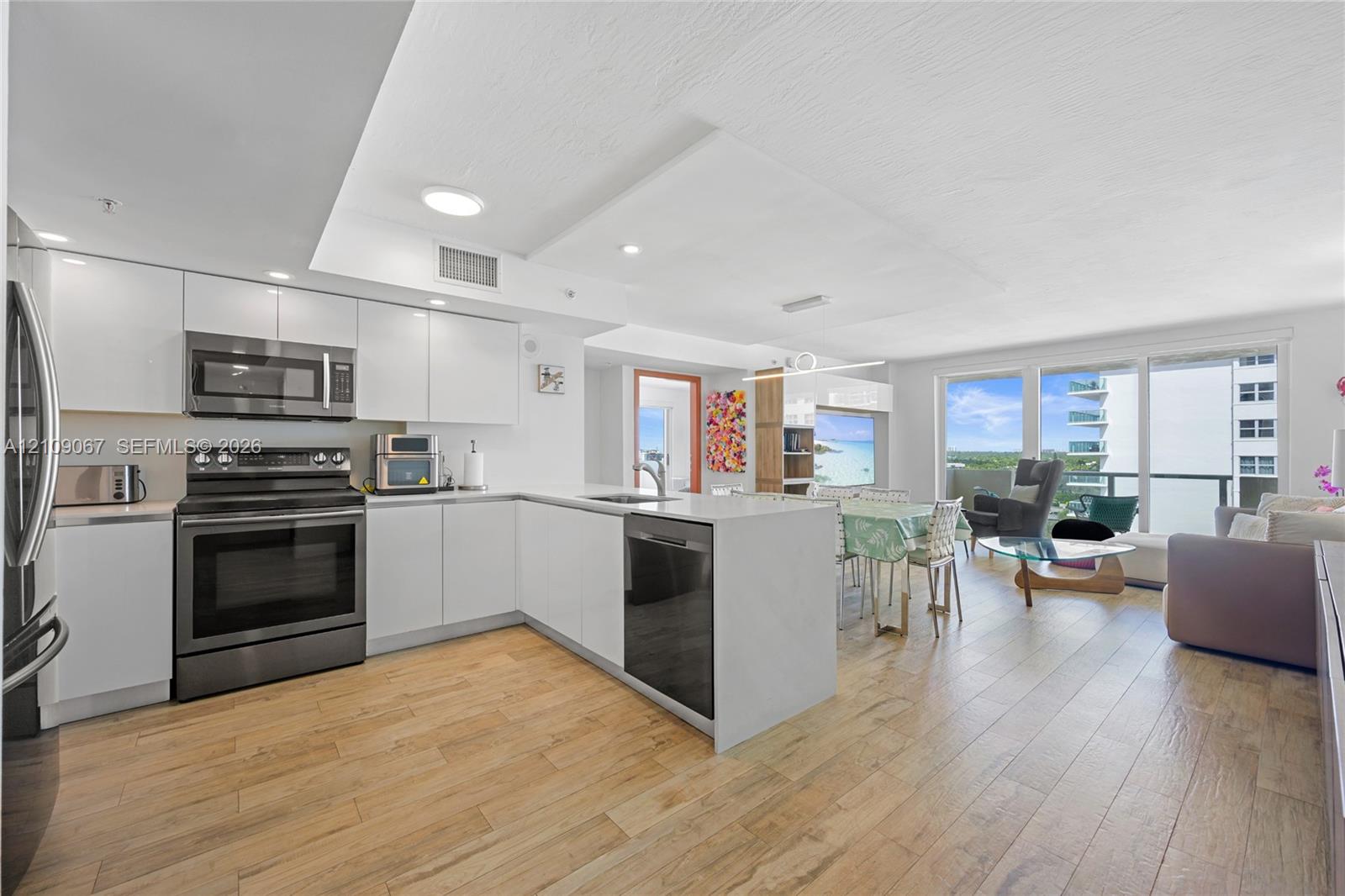 Modern kitchen featuring white flat-panel cabinetry, wood-finish flooring, quartz countertops, stainless steel appliances, and glass sliding doors Modern kitchen featuring white flat-panel cabinetry, wood-finish flooring, quartz countertops, stainless steel appliances, and glass sliding doors