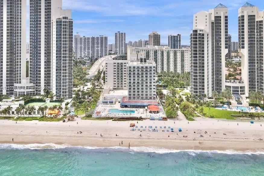 Direct oceanfront positioning featuring a swimming pool, paved sundeck, expansive sandy shoreline, and mature landscaping