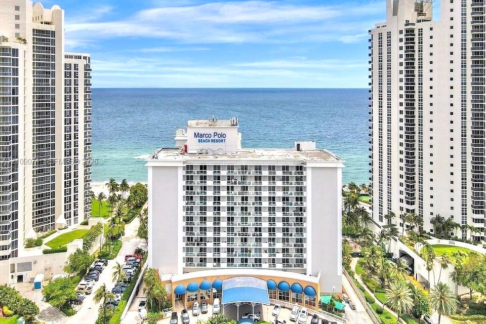 High-rise exterior featuring stacked private balconies, a covered porte-cochre, and coastal horizon backdrop