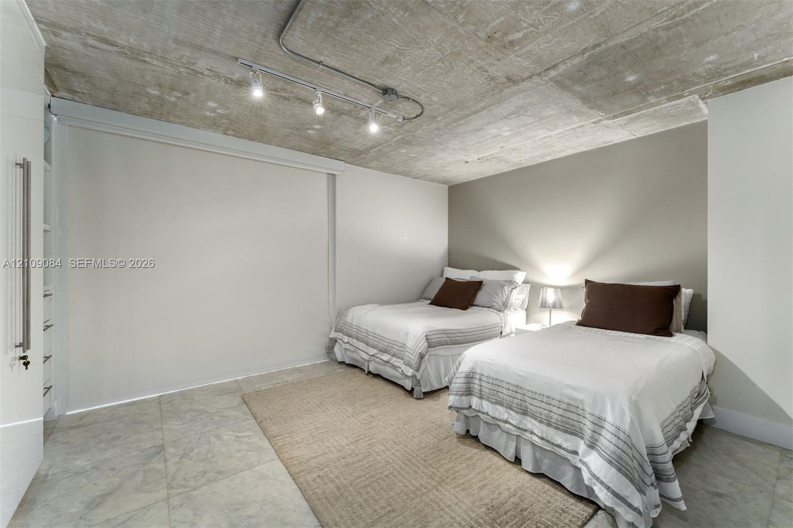 Exposed concrete ceiling with industrial-style track lighting, large-format tile flooring, and custom built-in floor-to-ceiling storage cabinetry
