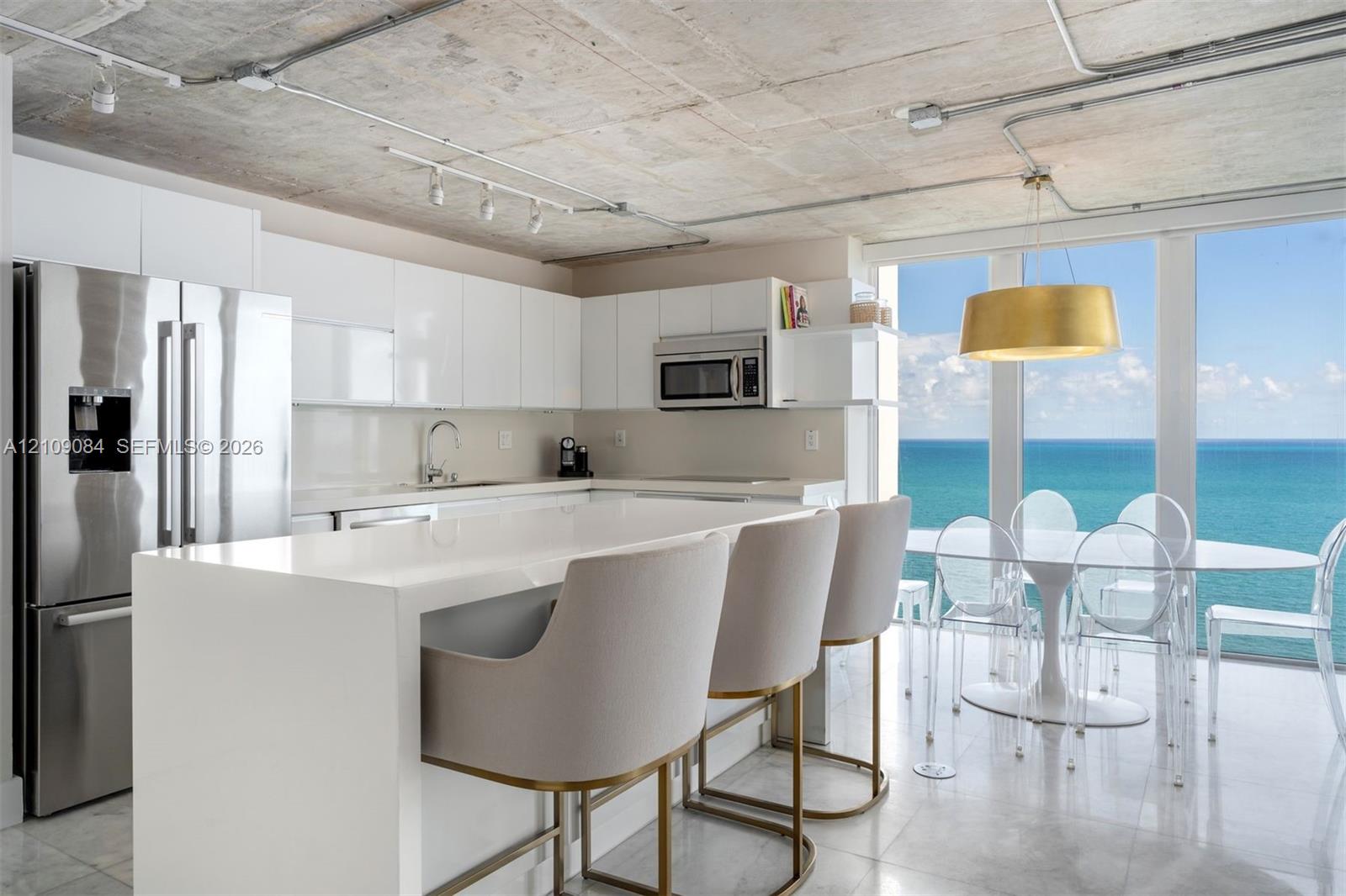 Exposed concrete ceiling, floor-to-ceiling glass paneling, stone-finish flooring, white flat-panel cabinetry, and a center island with a built-in wine refrigerator