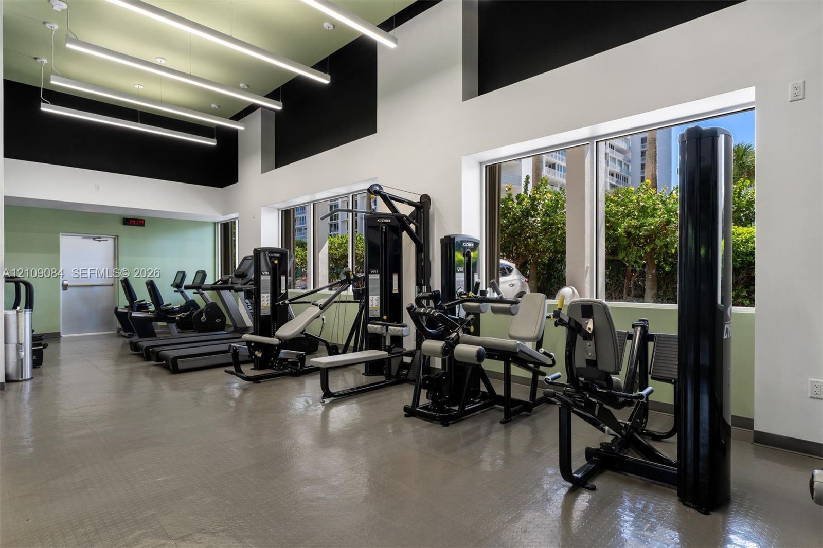 Fitness center featuring high ceilings, linear pendant lighting, large windows, and resilient flooring