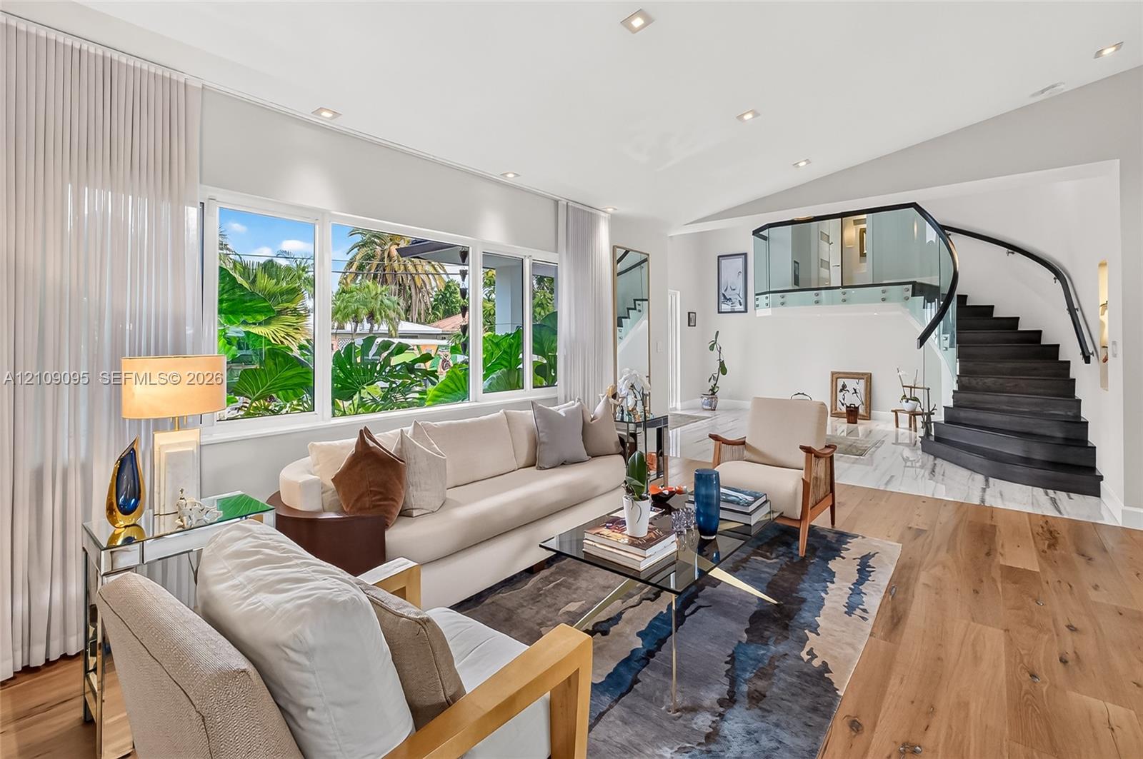 Vaulted ceilings with recessed lighting, floor-to-ceiling windows, wood-finish flooring, and a contemporary staircase with glass railing and dark wood treads