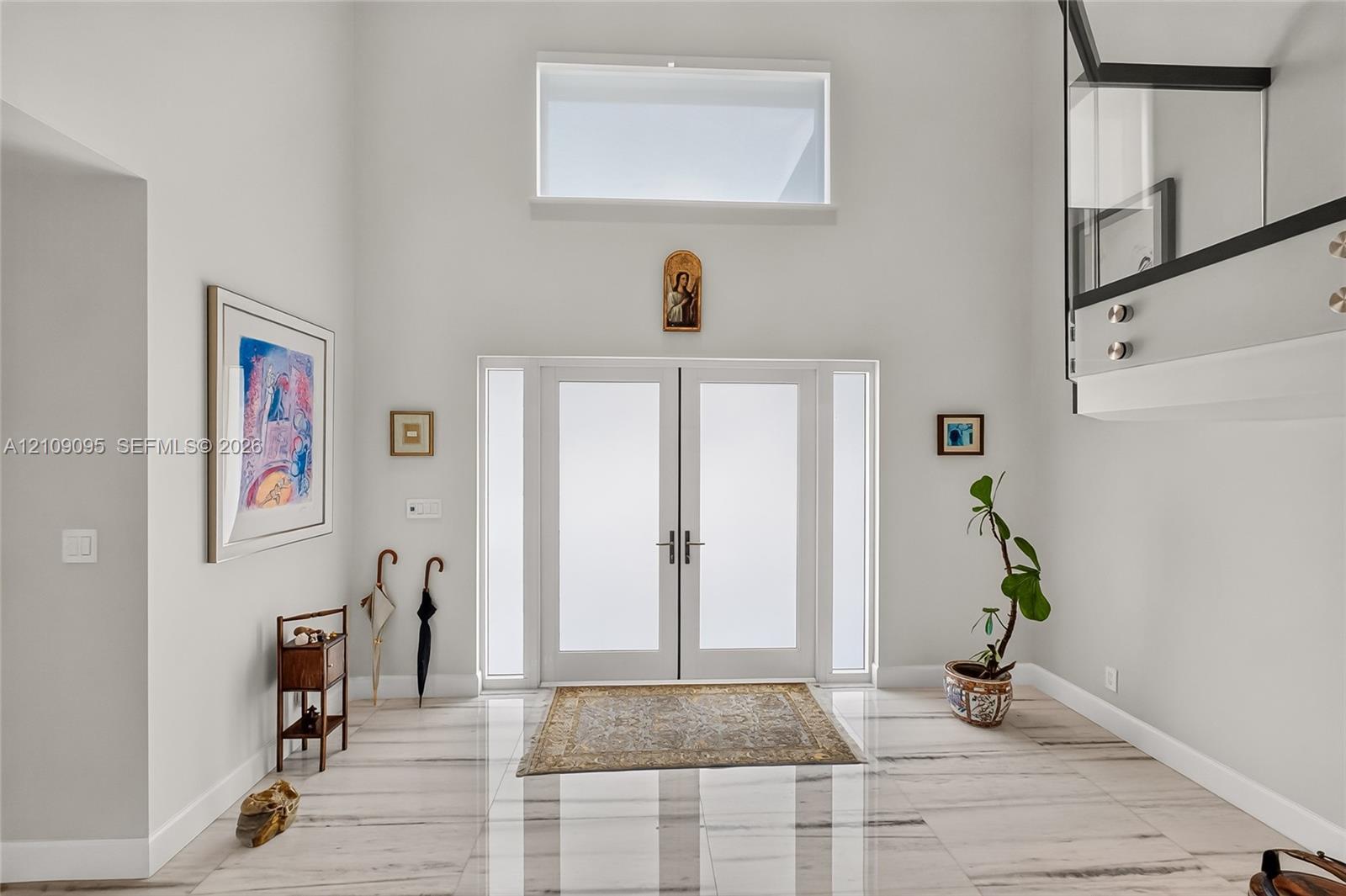 Double-height ceiling, glass-paneled entry door with frosted sidelights, upper-level clerestory window, stone-finish flooring, and glass stair railing with metal standoffs
