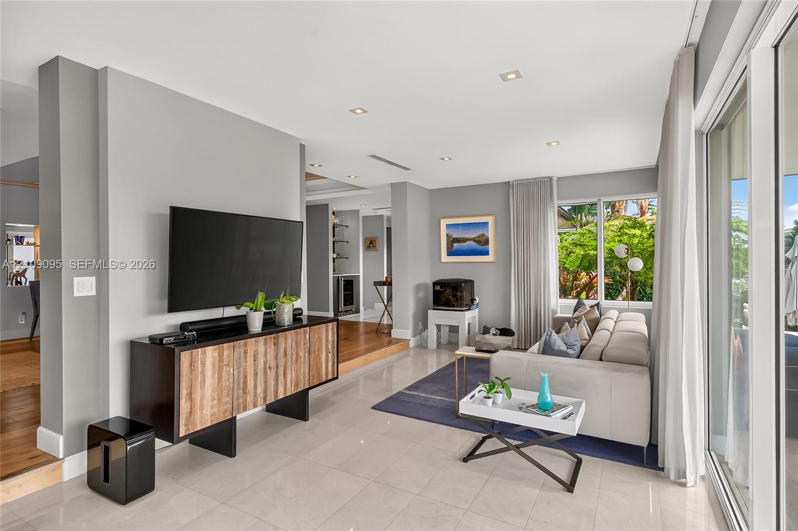 Living area featuring large-format tile flooring, recessed ceiling lighting, sliding glass doors, and stepped wood-finish flooring
