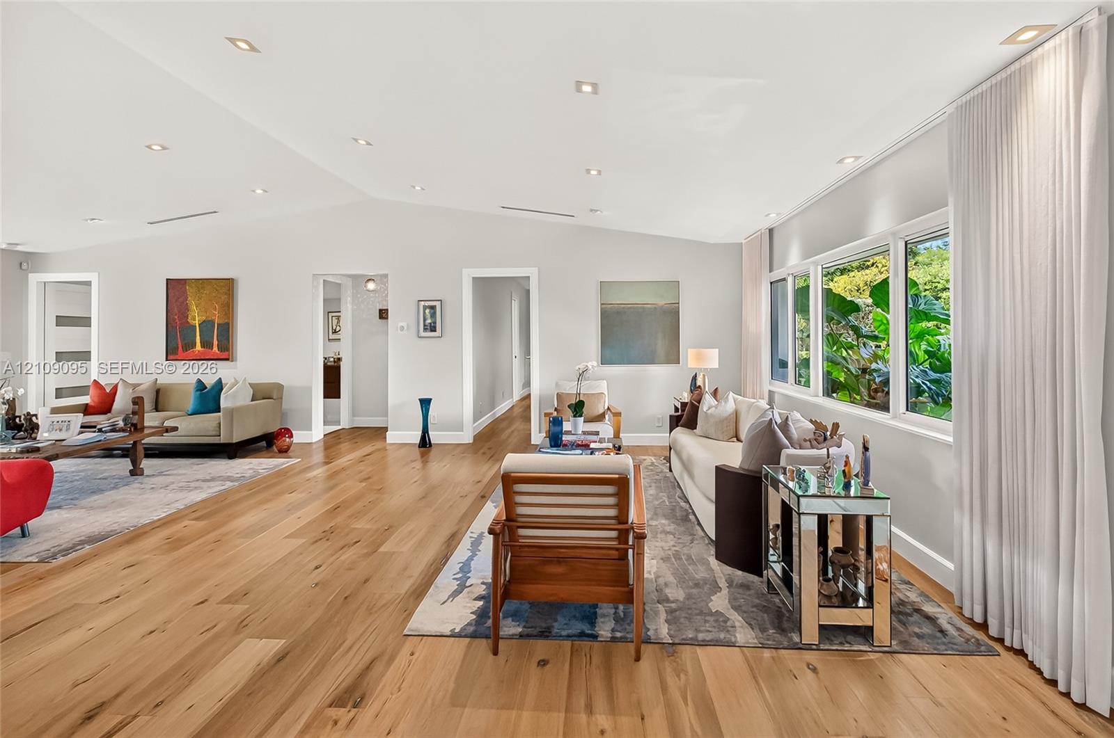 Open-concept living space featuring vaulted ceilings, wood-finish flooring, recessed lighting, and expansive windows