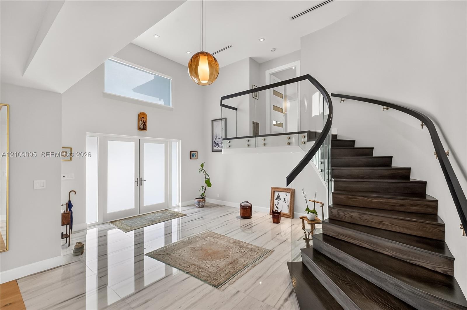 Double-height foyer featuring polished stone flooring, a curved staircase with dark wood-finish treads, and glass panel railing