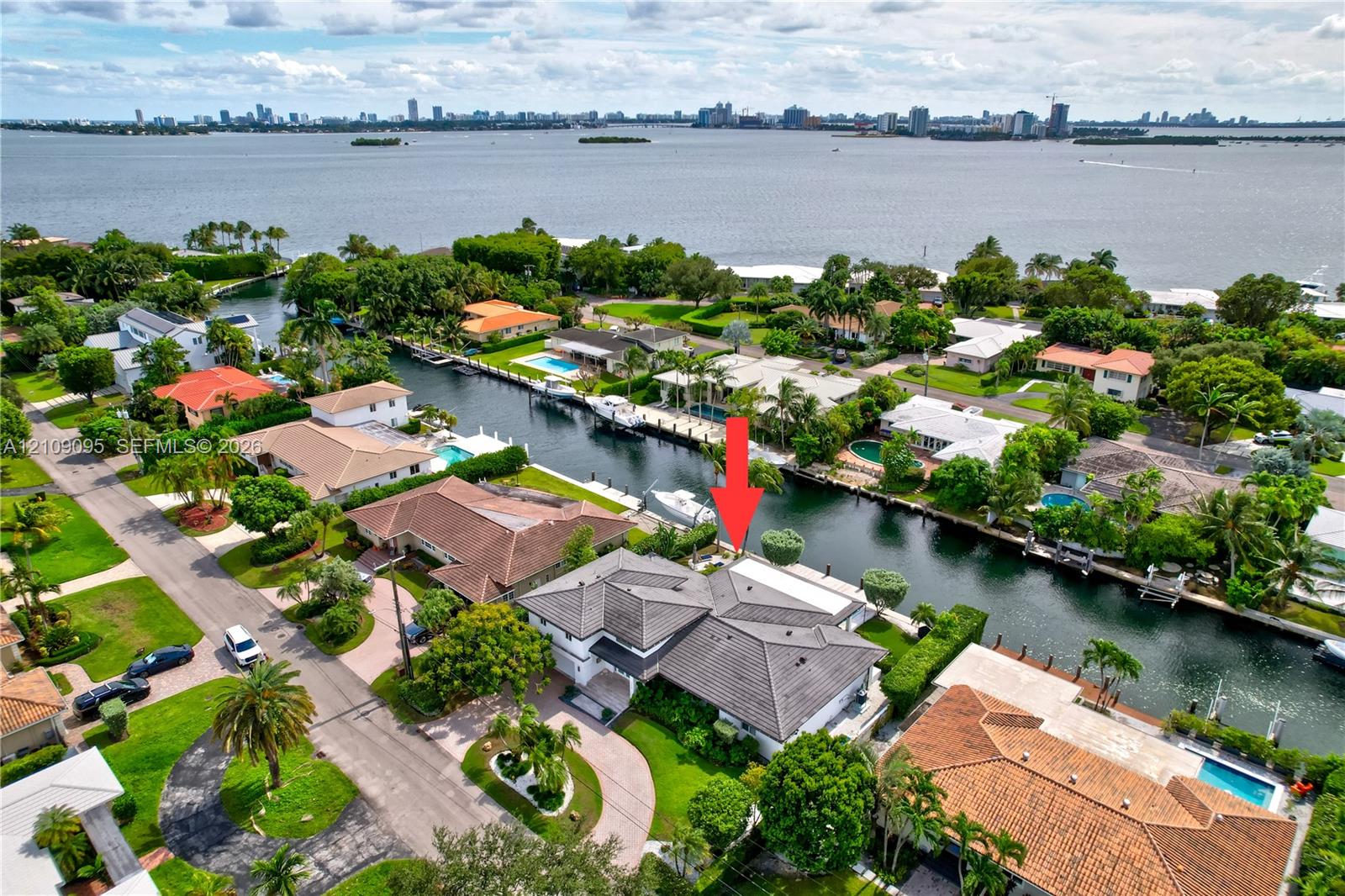 Waterfront property featuring a canal-side bulkhead, multi-gabled tile roof, paver driveway, and mature landscaping