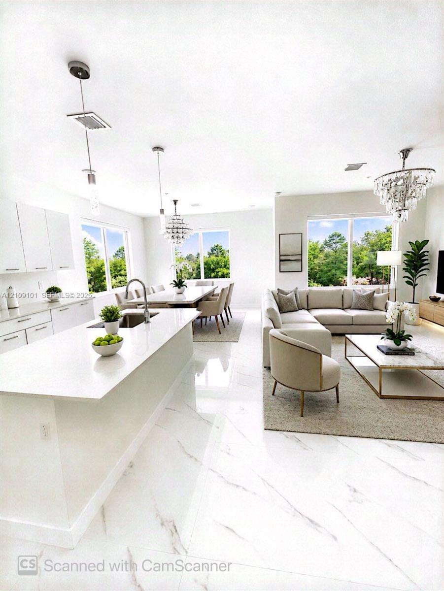 Open-concept interior featuring large-format tile flooring, a kitchen island with stone-finish countertops, crisp white cabinetry, and multi-light crystal chandeliers