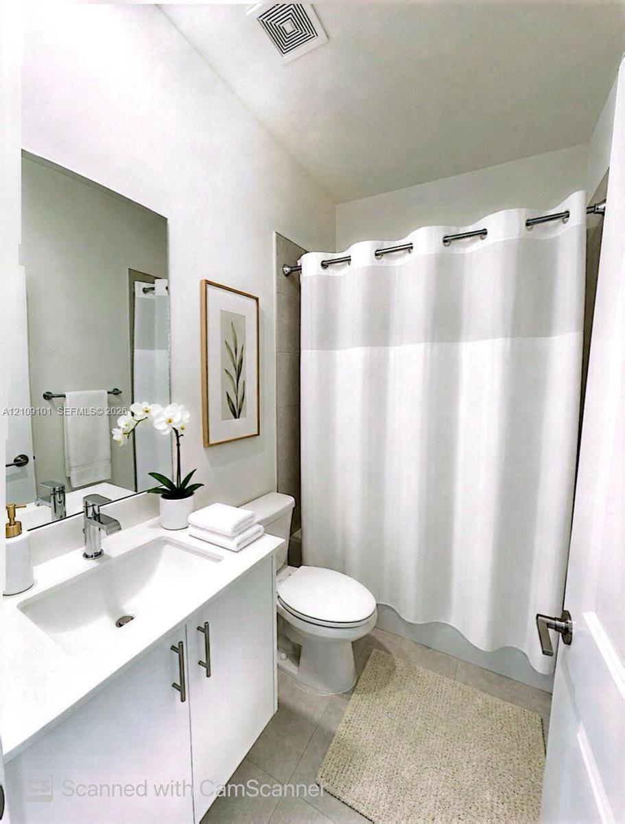 Bathroom featuring a white vanity cabinet, solid-surface countertop with an integrated sink, polished chrome faucet, full-width wall mirror, and a tile-surround shower