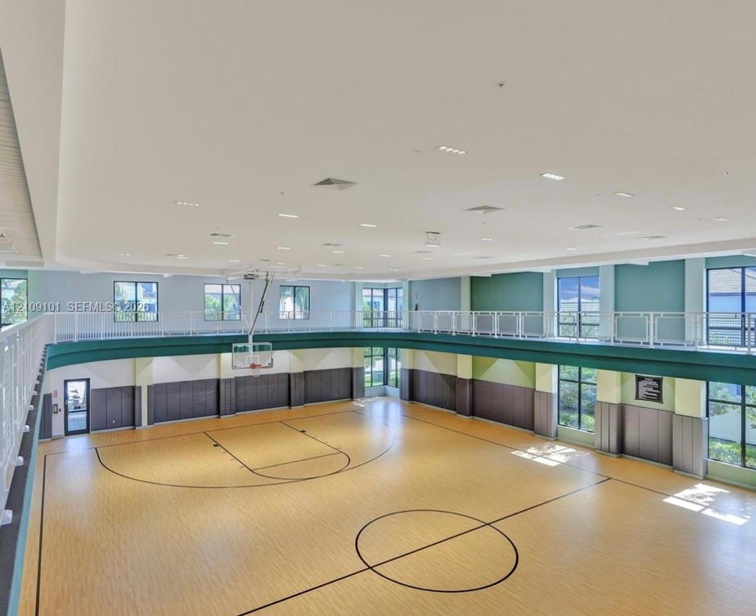 Indoor gymnasium featuring wood-finish flooring, a basketball hoop, multi-level spectator railing, recessed lighting, and expansive windows