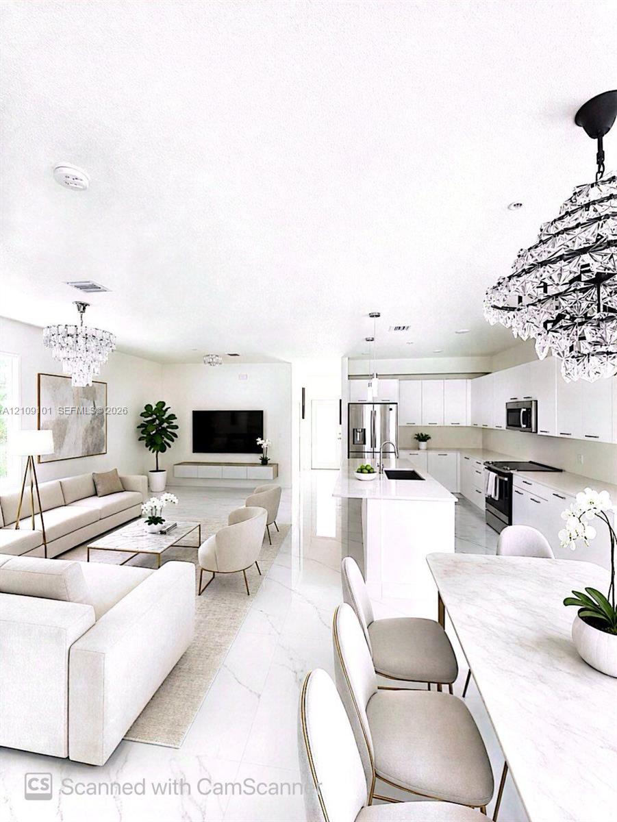 Open floor plan featuring large-format stone flooring, white shaker-style cabinetry, a central kitchen island with a stone countertop, and tiered crystal chandeliers