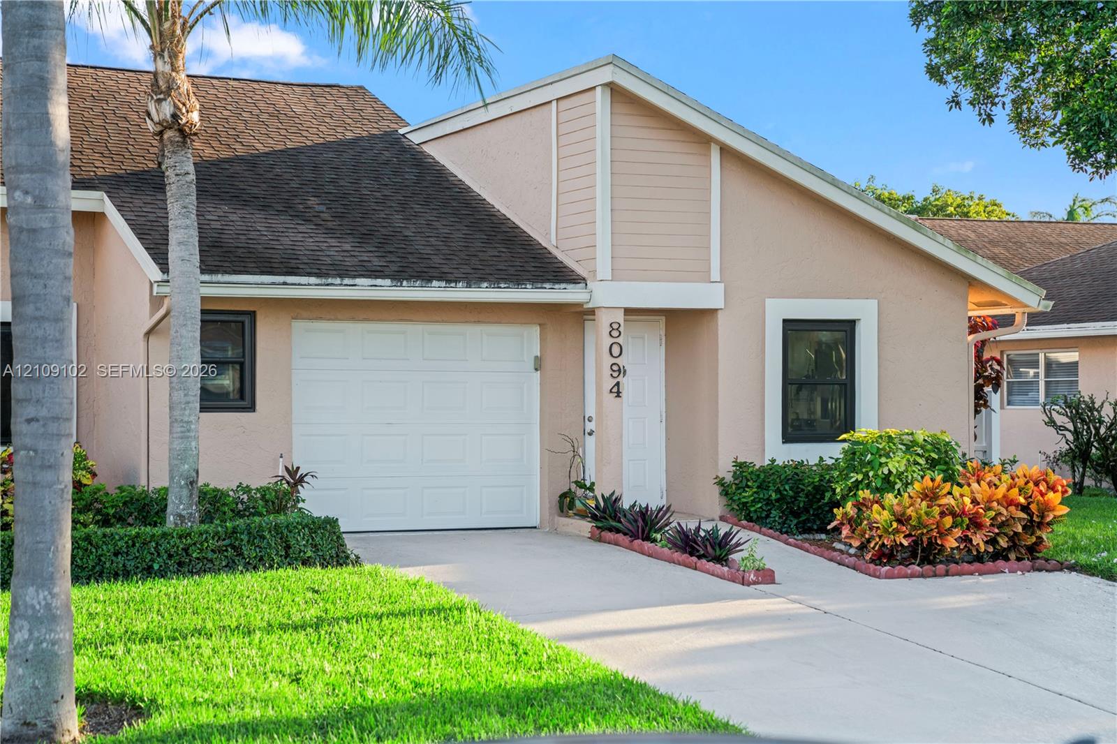 Stucco exterior featuring an attached one-car garage, concrete driveway, and landscaped garden beds