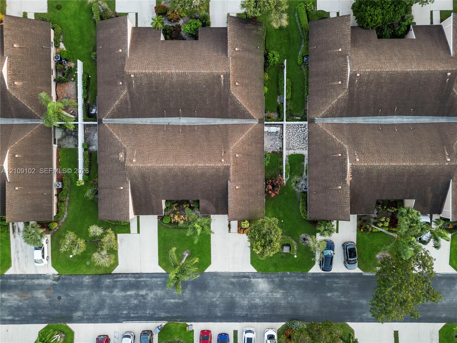 Aerial perspective featuring multi-unit structures with shingled roofs, paved driveways, established landscaping, and concrete walkways