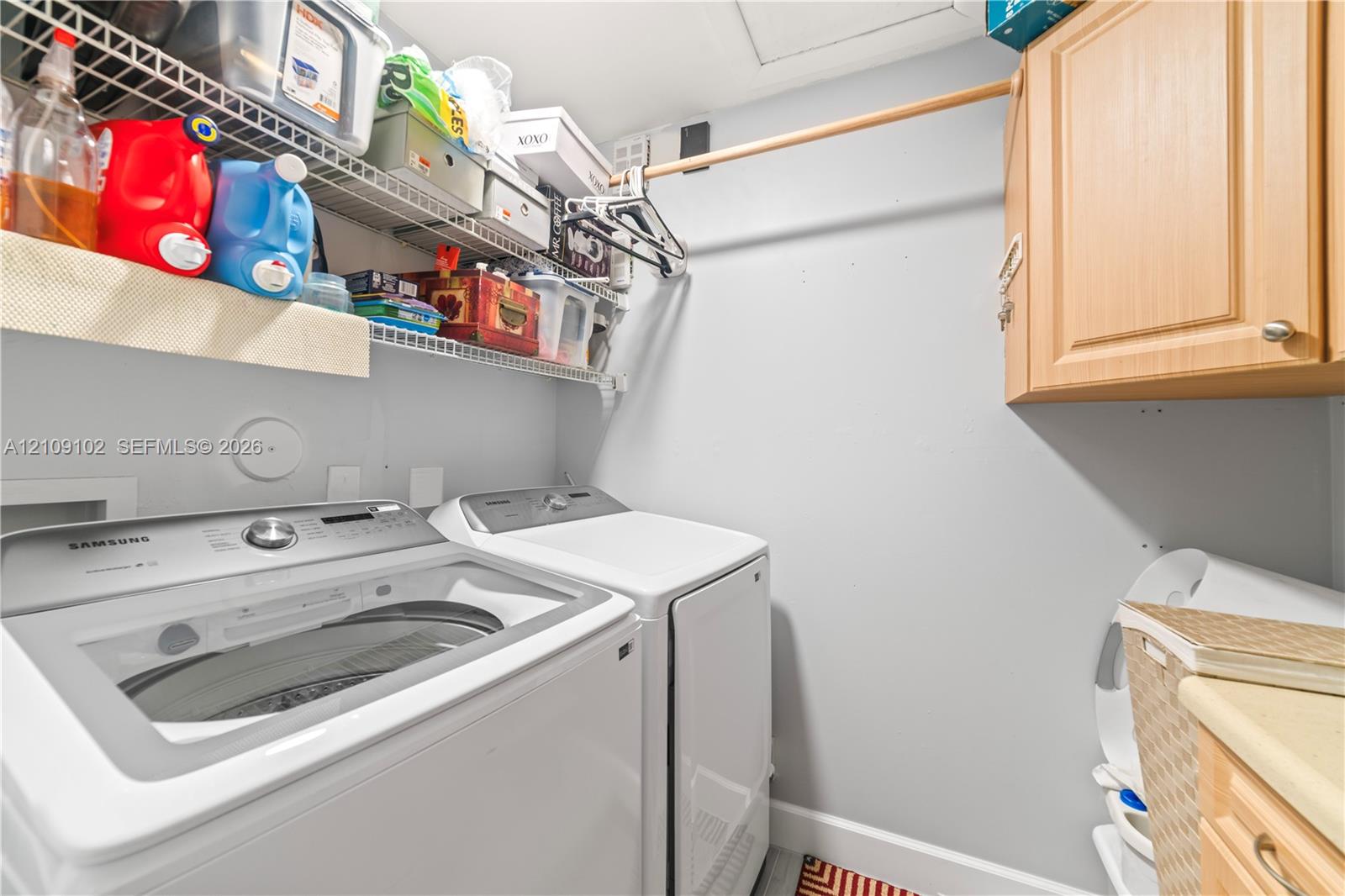 Laundry area featuring white top-load appliances, wall-mounted wood-finish cabinetry, and industrial-style wire shelving with an integrated hanging rod