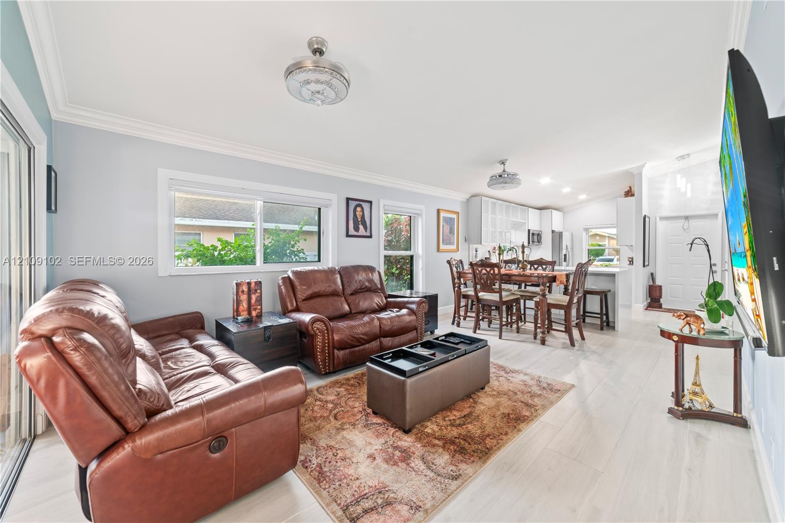 Open-concept living space featuring wood-finish flooring, recessed lighting, crown molding, dual ceiling fans, and sliding glass door access