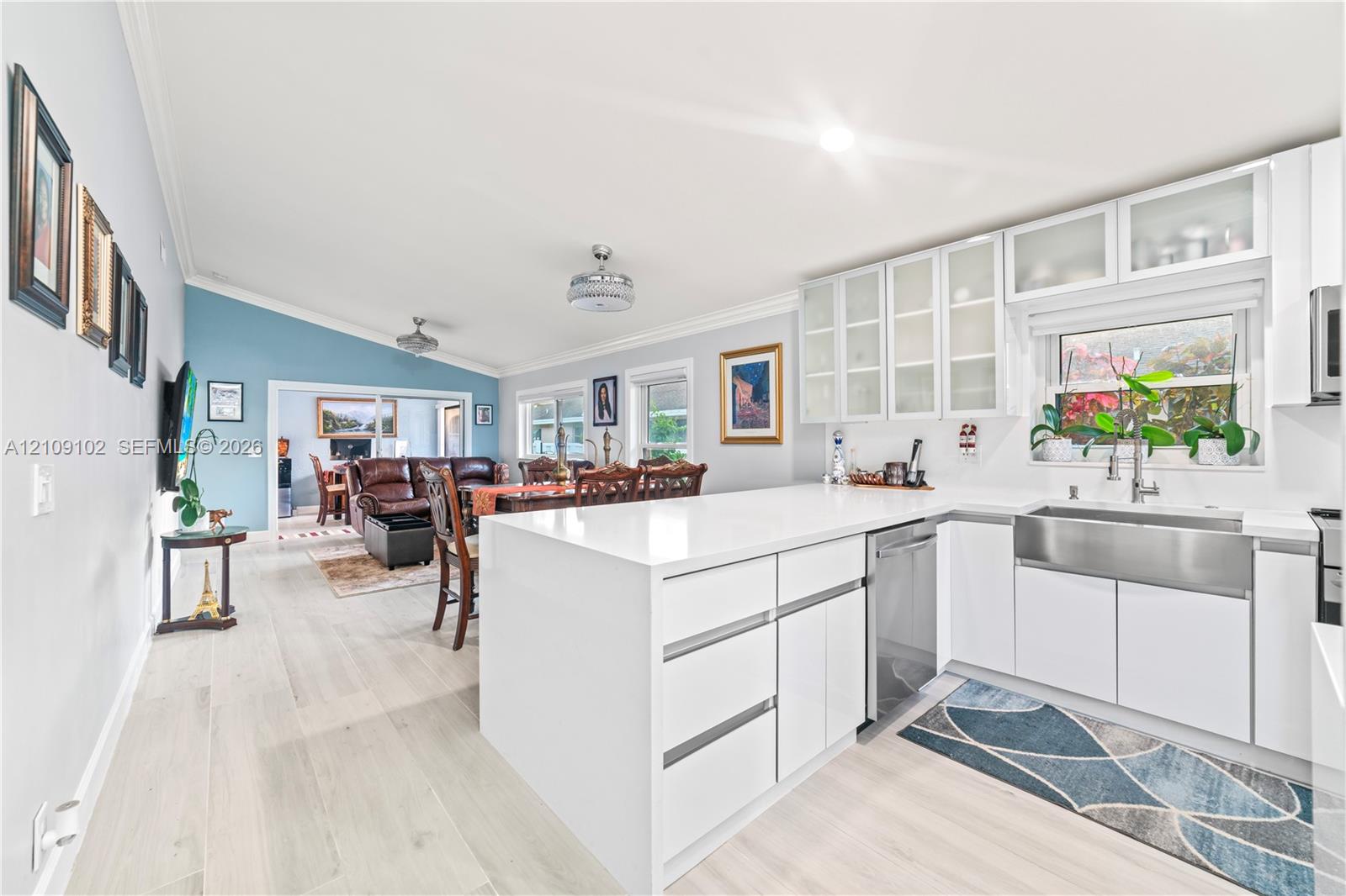 Kitchen featuring a solid surface peninsula, white flat-panel cabinetry with glass-front uppers, stainless steel apron-front sink, and wood-finish flooring
