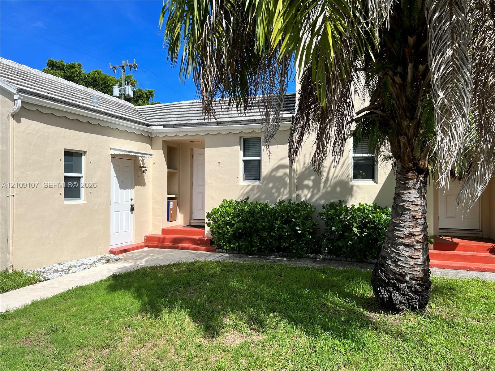 Exterior facade featuring a stucco finish, shingled roofing with scalloped eaves, concrete entry steps, and mature palm tree