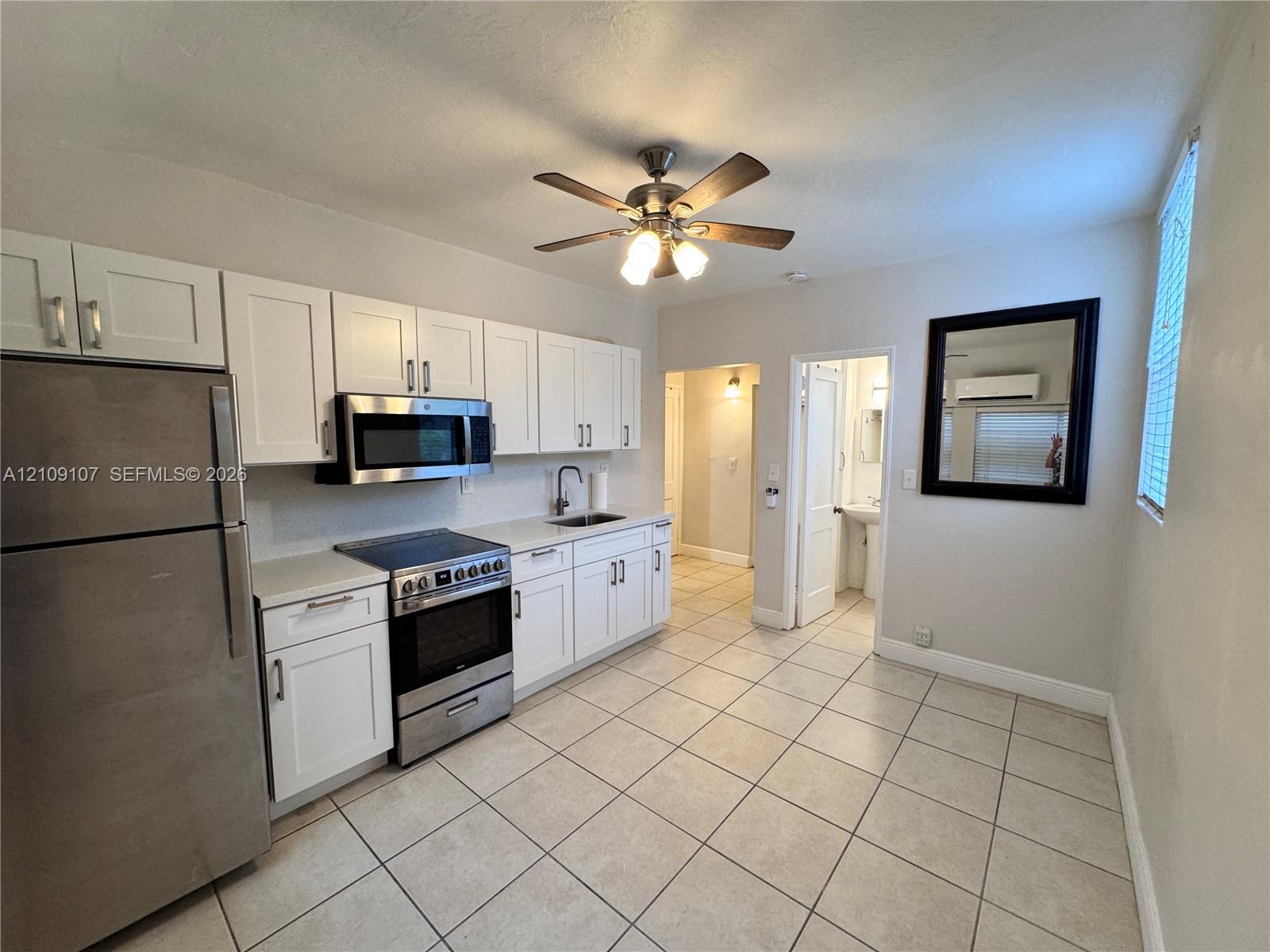 Kitchen featuring white shaker-style cabinetry, stainless steel appliances, neutral tile flooring, and a ceiling-mounted fan with integrated lighting