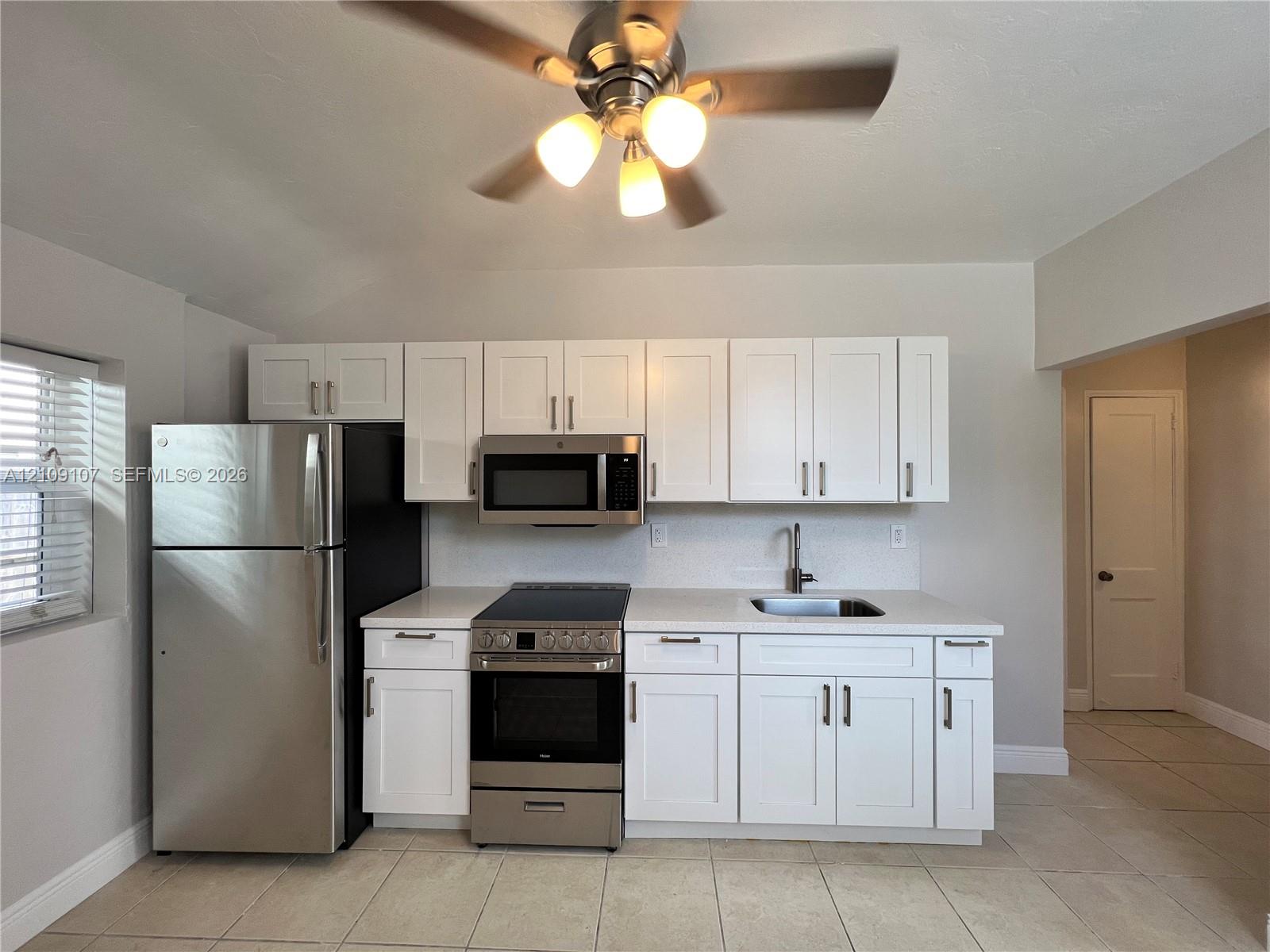 Kitchen featuring white shaker-style cabinetry, stainless steel appliances, neutral countertops, and tile flooring Kitchen featuring white shaker-style cabinetry, stainless steel appliances, neutral countertops, and tile flooring