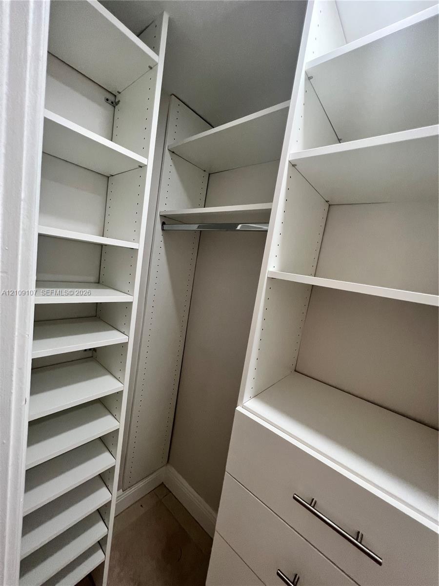 Walk-in closet featuring white built-in shelving, adjustable storage racks, a metal hanging rod, and drawers with metallic bar pulls