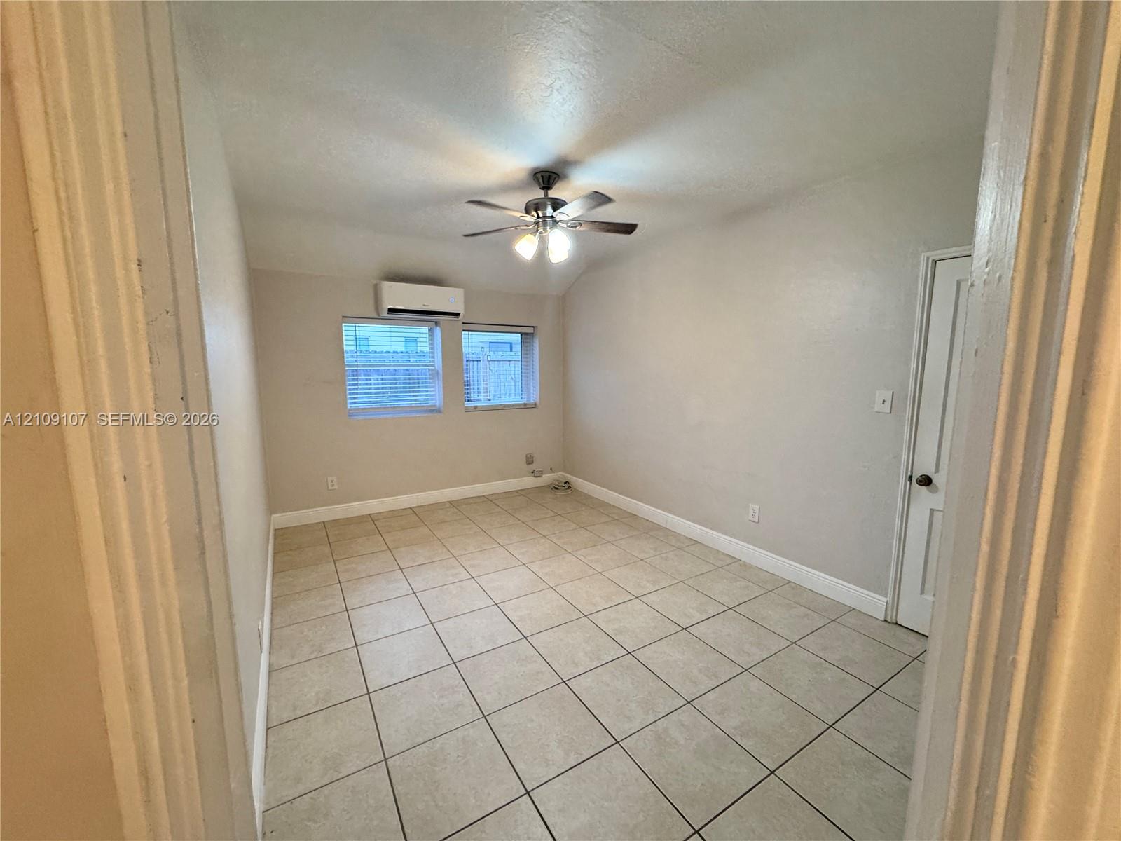 Interior room featuring neutral tile flooring, a dual-light ceiling fan, and a wall-mounted ductless climate control unit