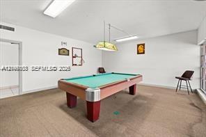 Interior space featuring neutral-toned carpeting, rectangular recessed overhead lighting, and a hanging geometric light fixture