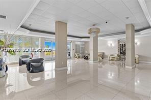 Expansive lobby featuring polished tile flooring, tray ceilings with recessed lighting, structural support columns, wall-mounted accent lighting, and floor-to-ceiling glass paneling