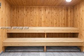 Sauna featuring wood-paneled walls, multi-level built-in wood benches, and tiled flooring