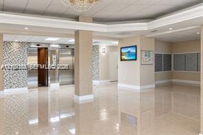 Lobby featuring polished tile flooring, metallic elevators with decorative tile surrounds, recessed lighting, and a tiered crystal chandelier