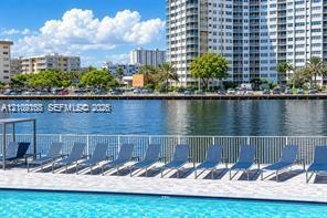 Waterfront swimming pool area featuring a paved deck, perimeter metal fencing, and water-level bulkhead