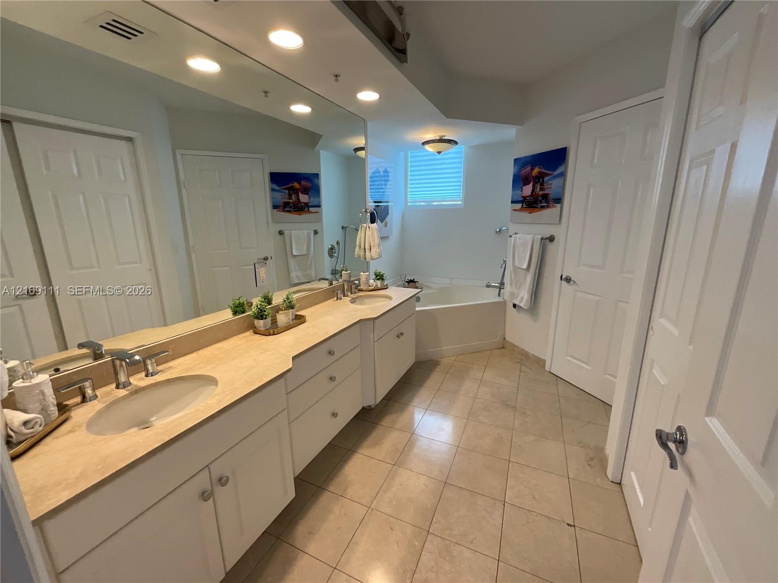 Dual-sink vanity with stone countertop, recessed lighting, tile flooring, and integrated soaking tub