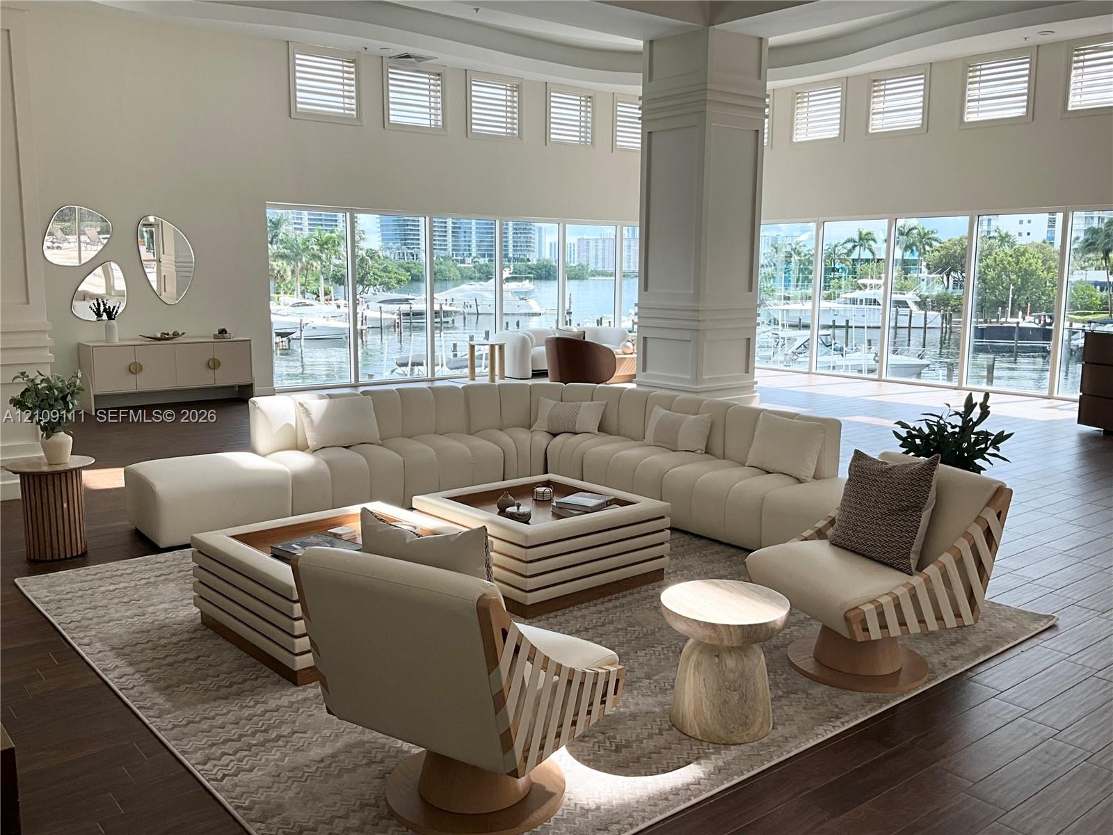 Expansive living area featuring floor-to-ceiling windows, dark wood-finish flooring, soaring ceilings, and a central architectural pillar