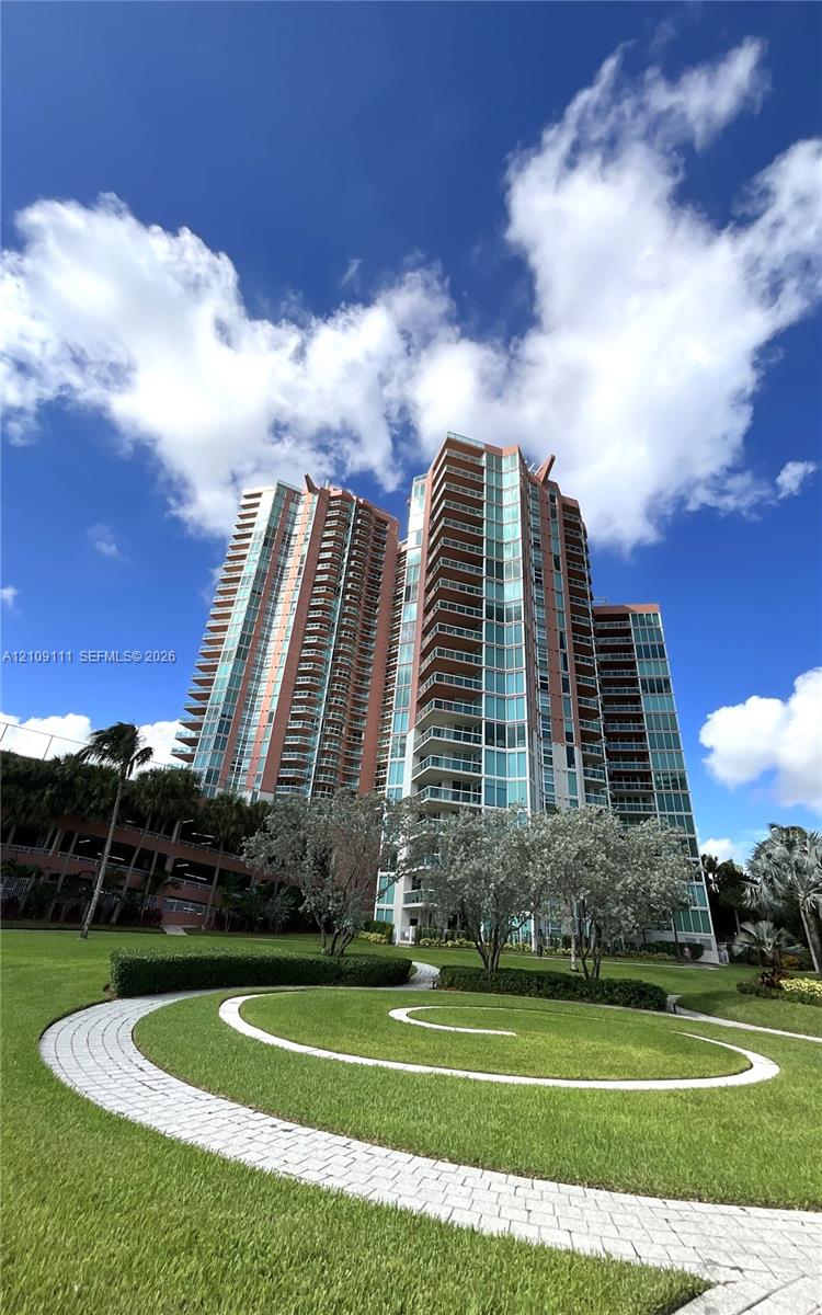 High-rise residential structure featuring glass facades and wrap-around balconies, complemented by landscaped grounds, manicured lawns, and paved stone walkways