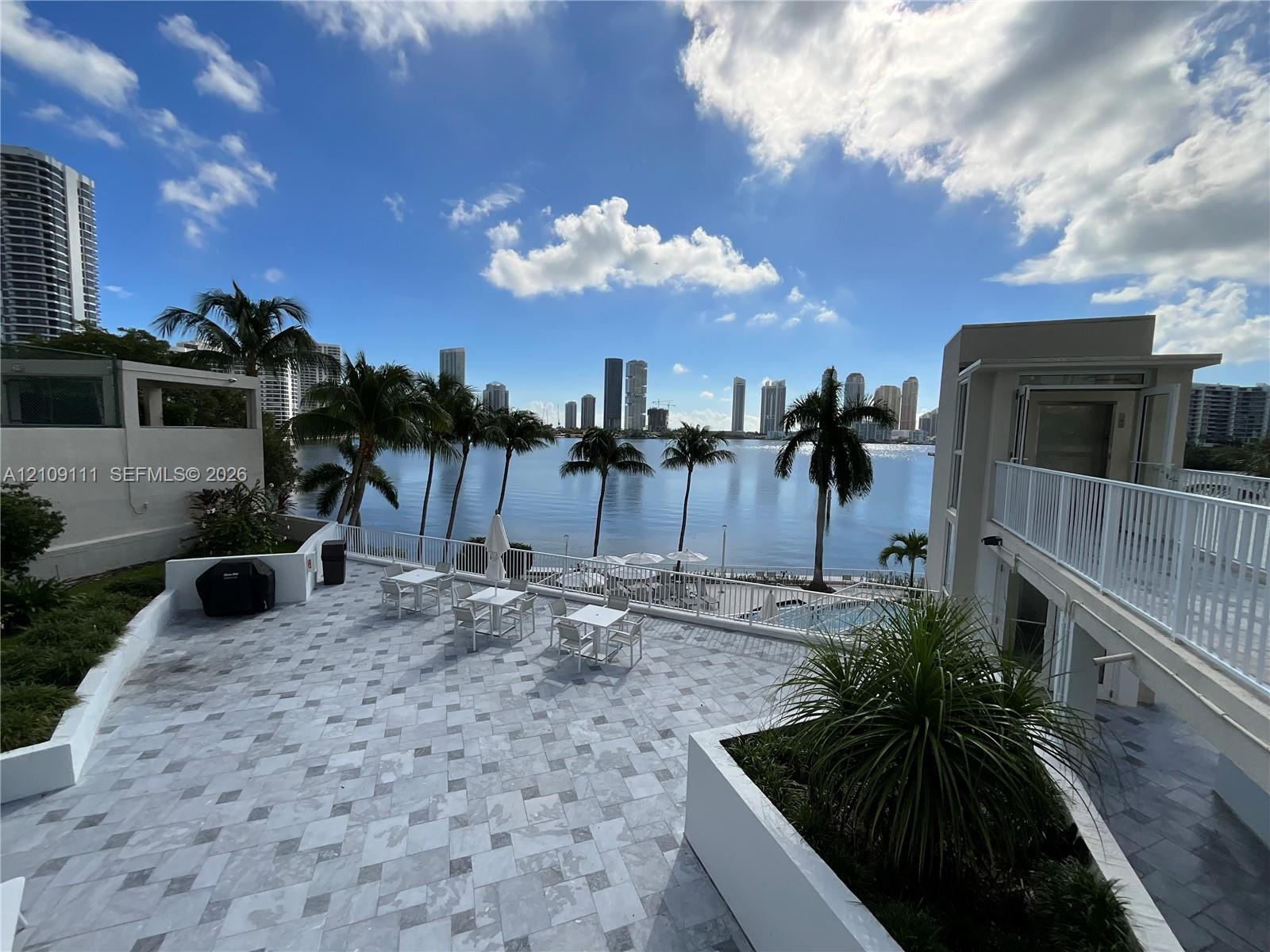 Expansive stone-paved terrace featuring white masonry planter boxes, perimeter metal railings, and elevated walkway access Expansive stone-paved terrace featuring white masonry planter boxes, perimeter metal railings, and elevated walkway access