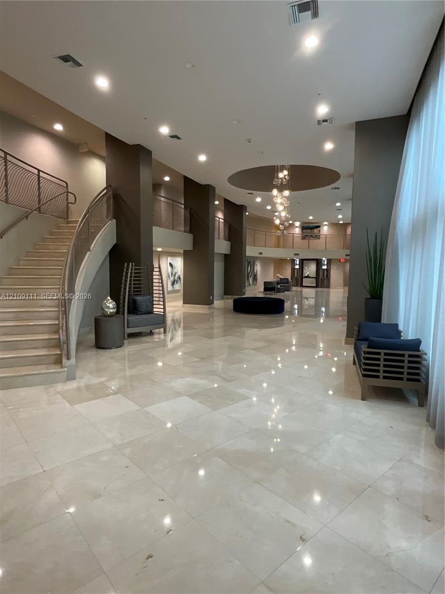 Grand entrance hall featuring high ceilings, stone tile flooring, a multi-tiered glass chandelier, a sweeping staircase with custom metal railings, and a tiered mezzanine level Grand entrance hall featuring high ceilings, stone tile flooring, a multi-tiered glass chandelier, a sweeping staircase with custom metal railings, and a tiered mezzanine level