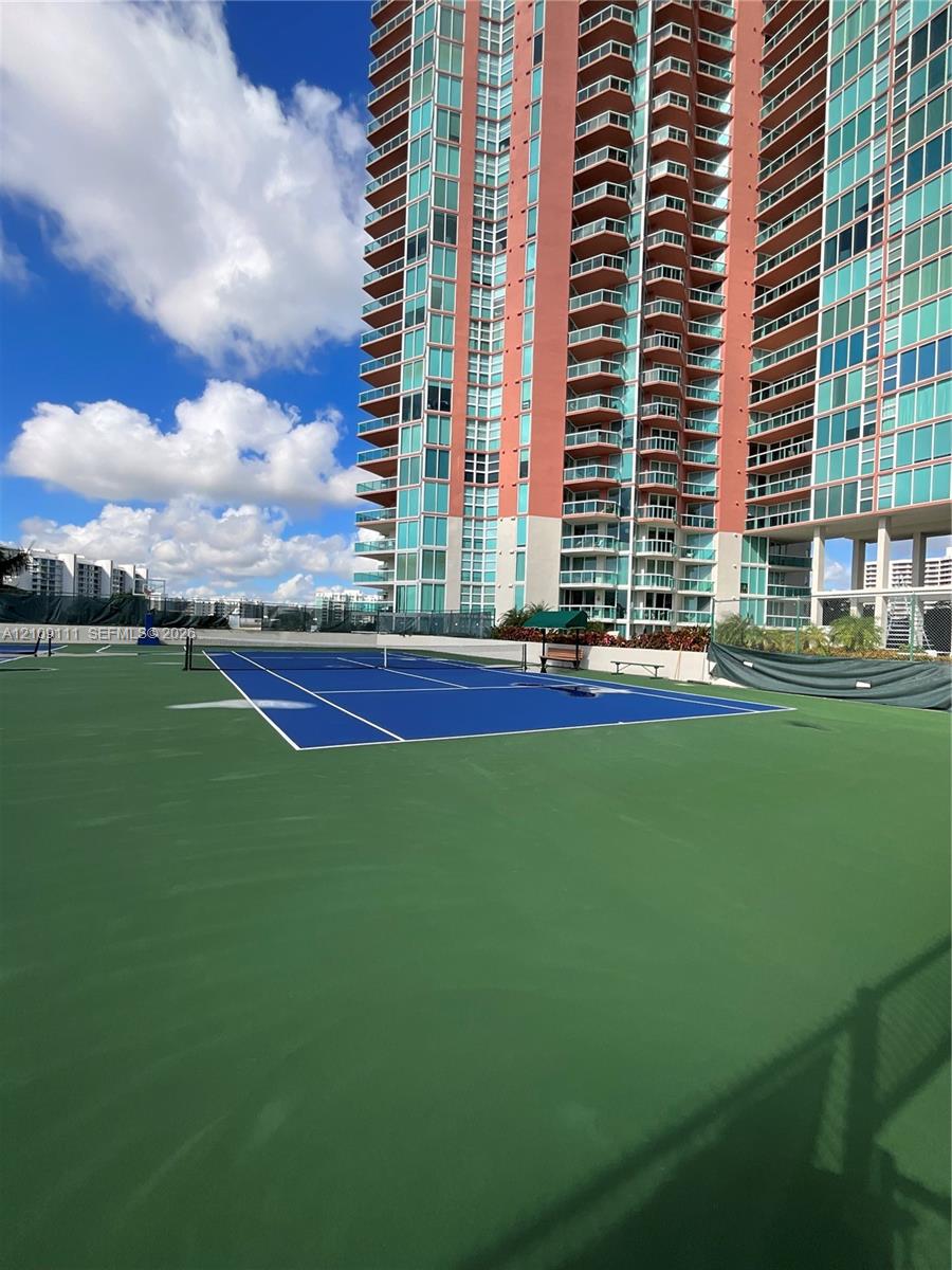 Recreational tennis court with blue and green surfacing, enclosed by high fencing and protective mesh screens