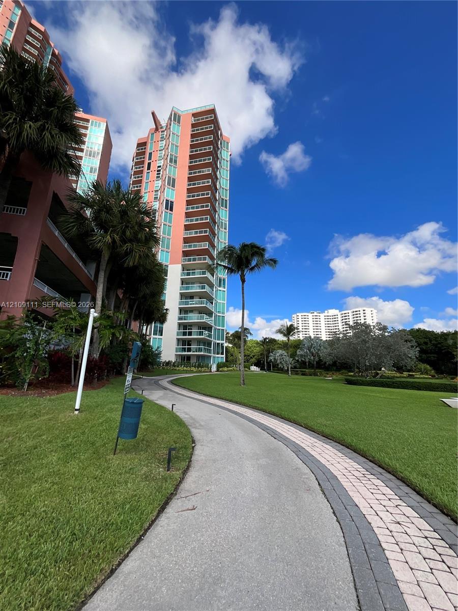 High-rise building with multiple private balconies, landscaped lawn, and paved stone walking path