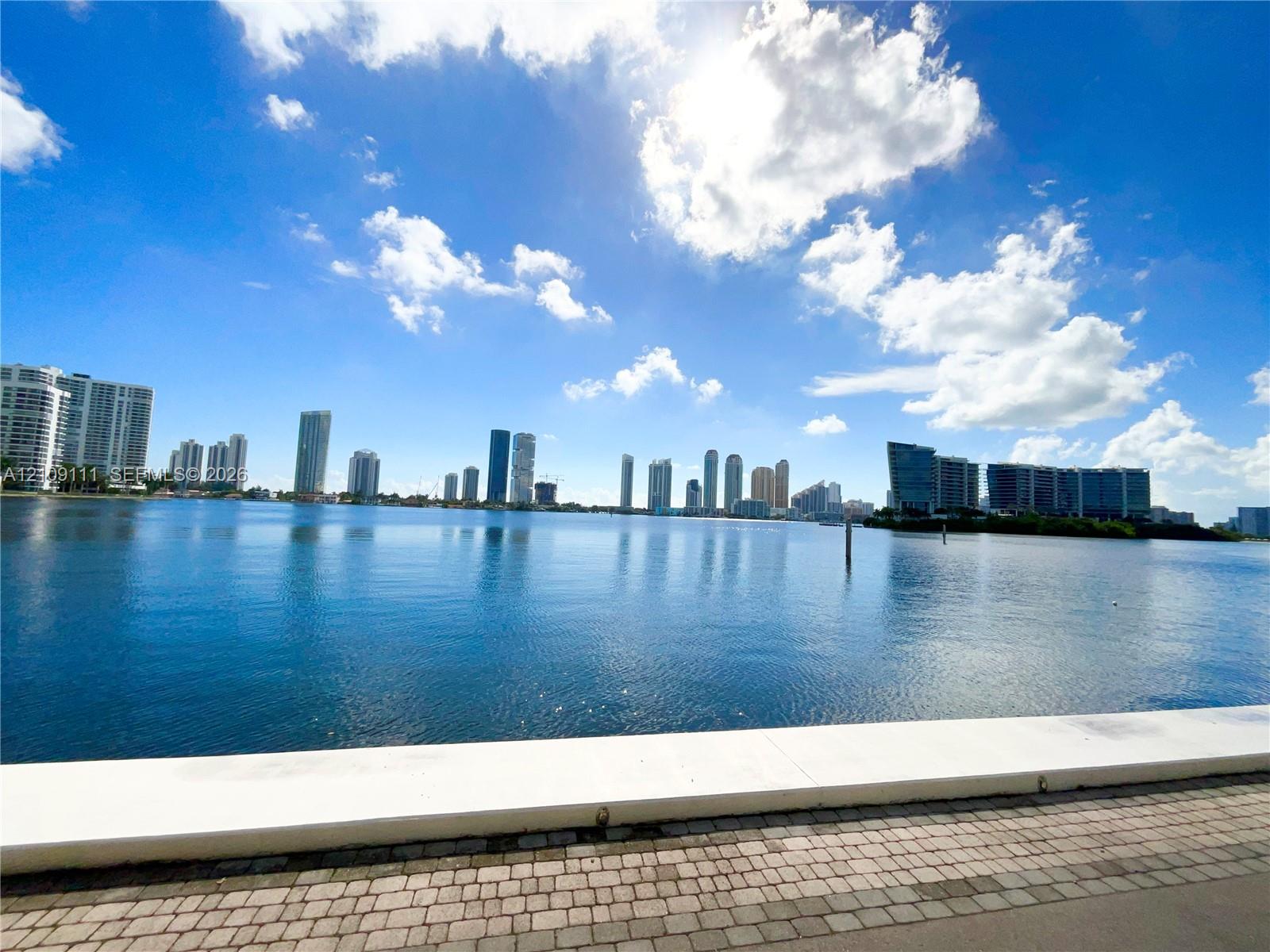 Waterfront property featuring a concrete seawall, paver-lined walking path, and a backdrop of city skyline