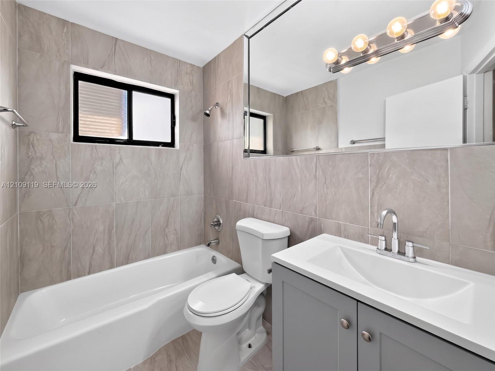 Bathroom featuring floor-to-ceiling large-format tile, gray vanity with a white composite countertop, integrated sink, and full-width vanity mirror
