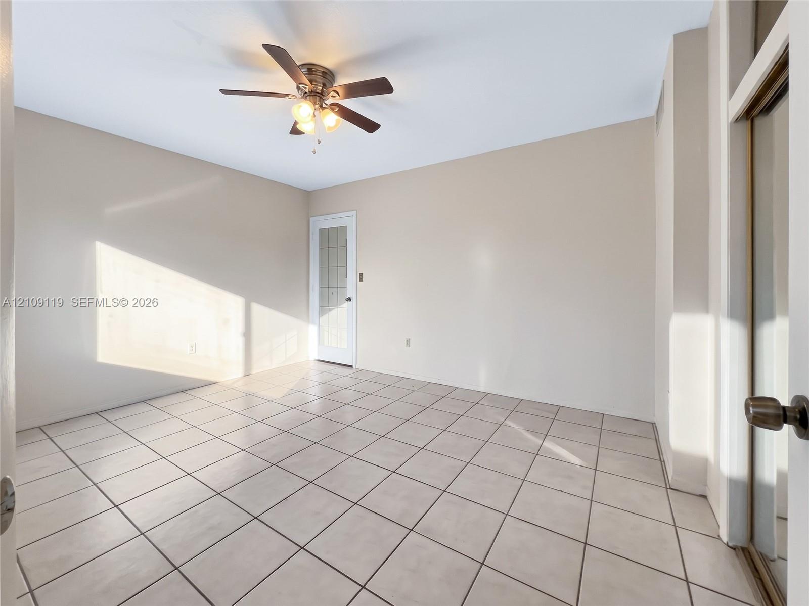 Neutral-toned interior space featuring light-colored square tile flooring, a multi-blade ceiling fan with integrated lighting, and a single-panel door with glass inserts