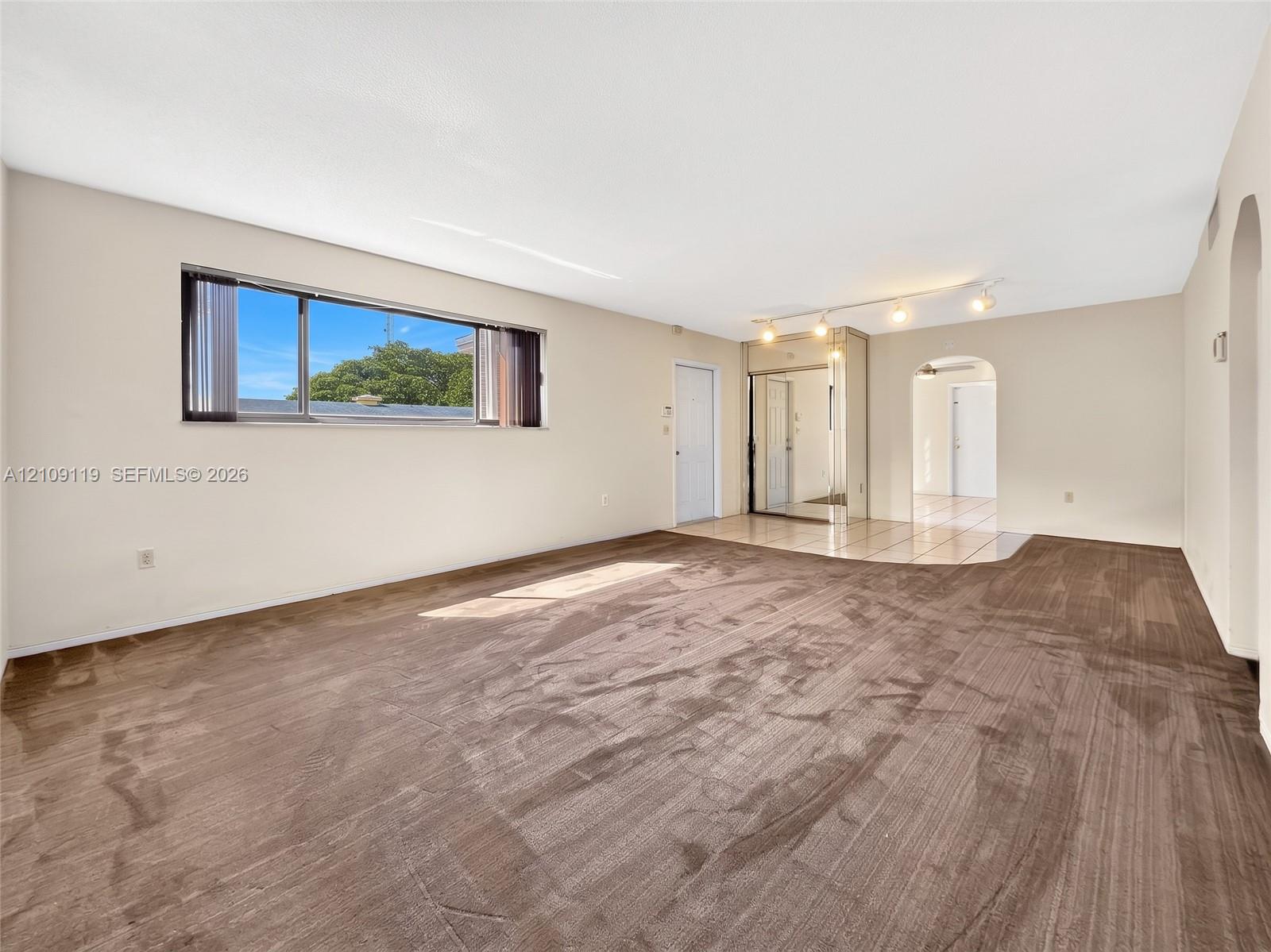 Neutral-toned interior featuring carpeting, a horizontal sliding window, a mirrored closet, ceramic tile flooring, and arched entryways