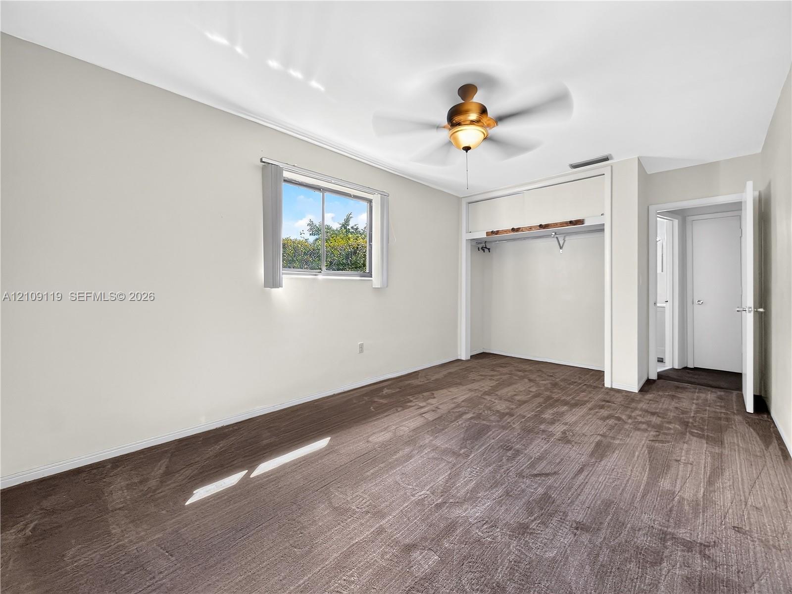 Neutral carpeting, recessed closet space with integrated shelving, sliding-sash window, and central ceiling fan with integrated light fixture