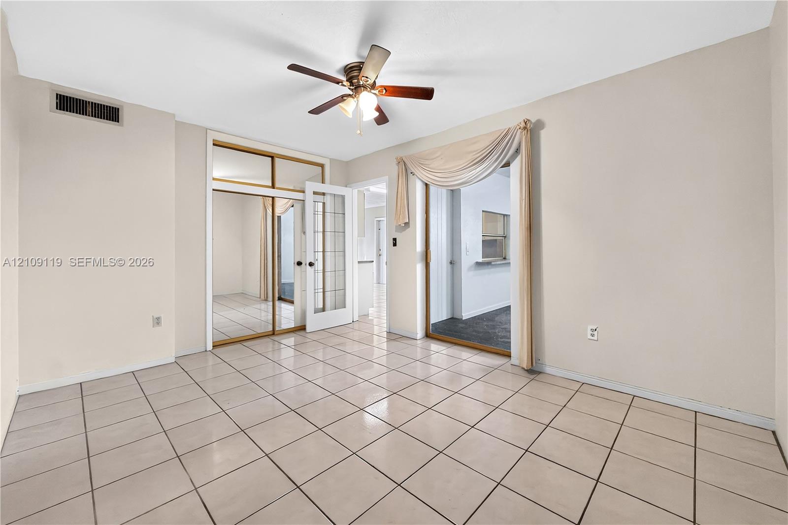 Interior space featuring light-toned tile flooring, a central ceiling fan with integrated lighting, a glass-paned French door, and a built-in closet with mirrored sliding doors