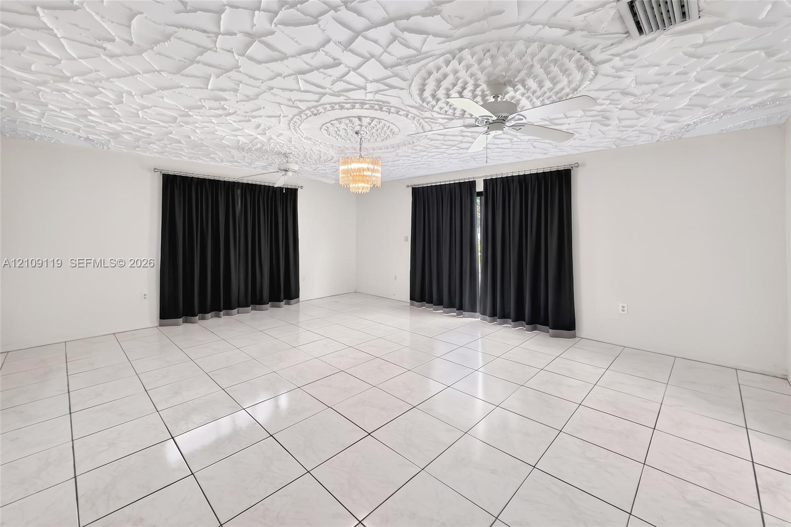 Expansive room featuring a textured decorative ceiling, dual ceiling fans, polished tile flooring, and a central tiered crystal chandelier