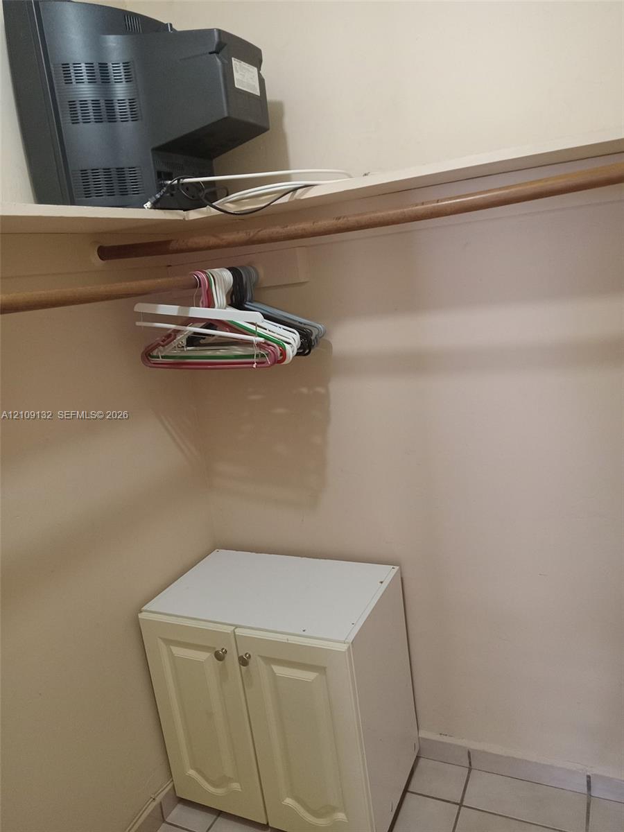Closet space featuring a built-in cabinet with dual cabinet doors and a mounted wood-finish hanging rod with an upper shelving unit