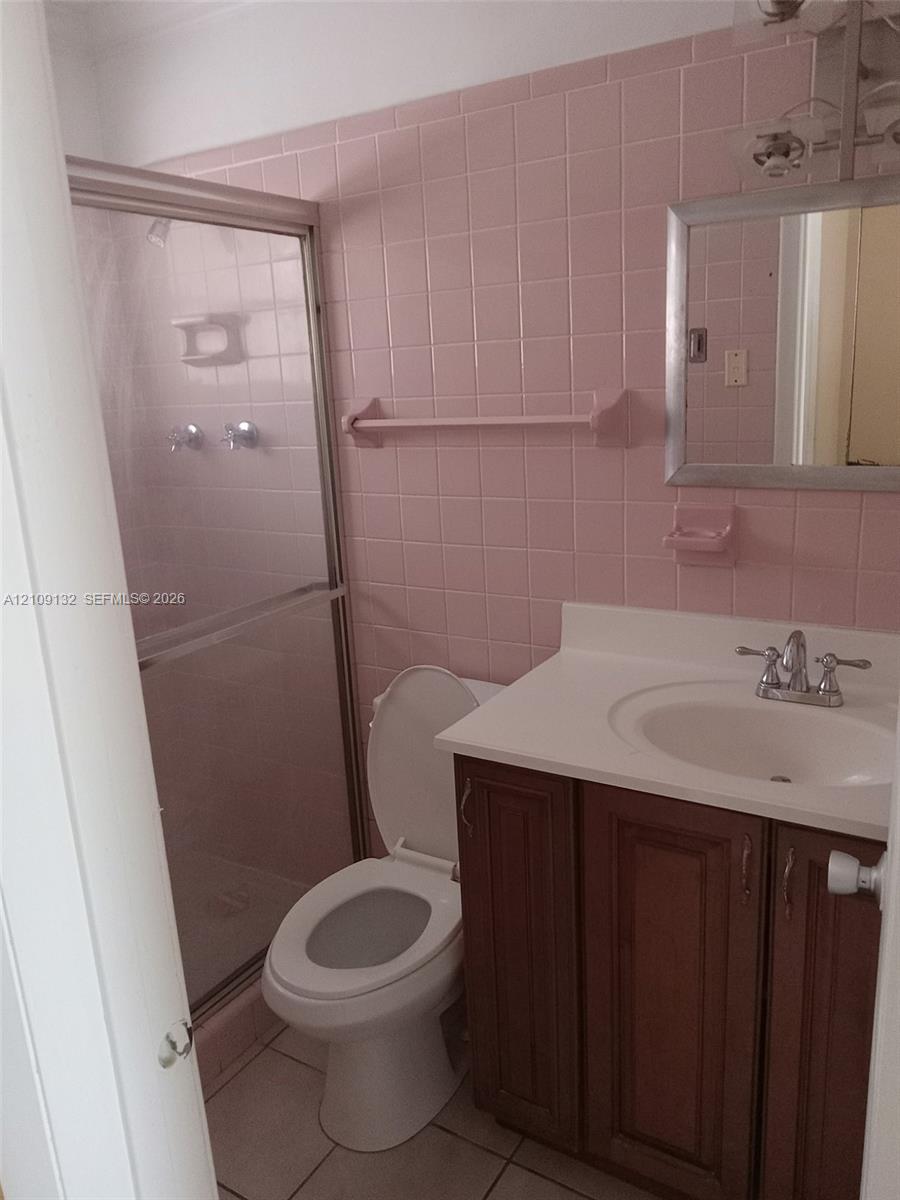 Full bathroom featuring square ceramic wall tiling, a vanity with a white countertop and drop-in sink, a shower enclosure with a sliding glass door, and tiled flooring